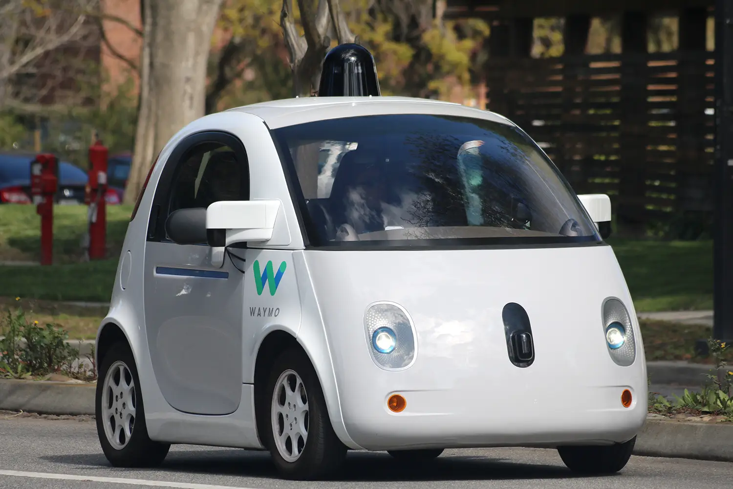 The small, distinctive Waymo car with cameras and sensors mounted to its roof and front side.